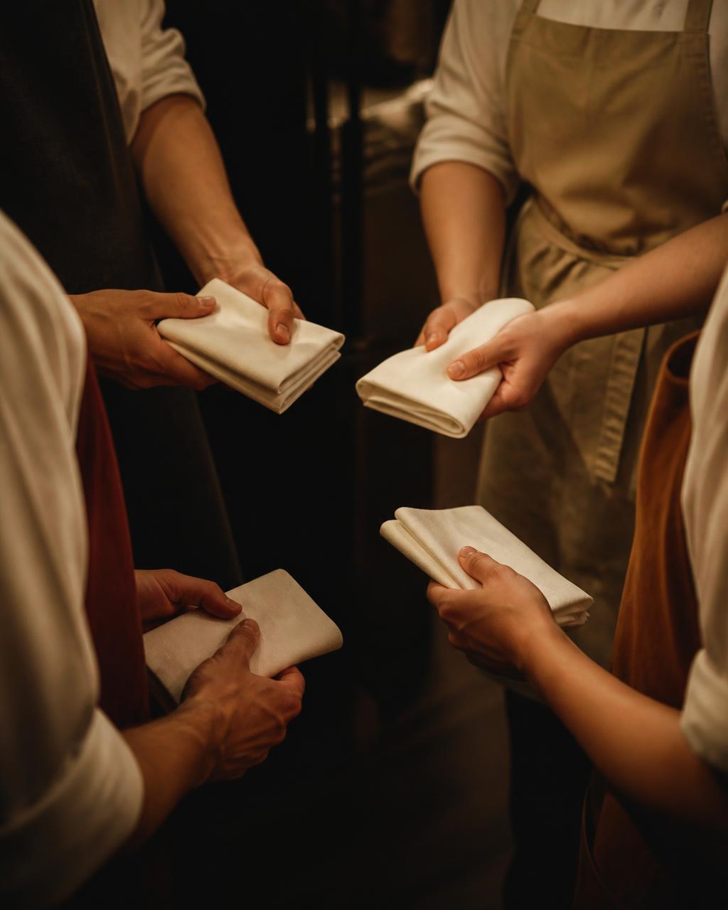 Restaurant staff hands passing folded white napkins during a pre-shift line-up.